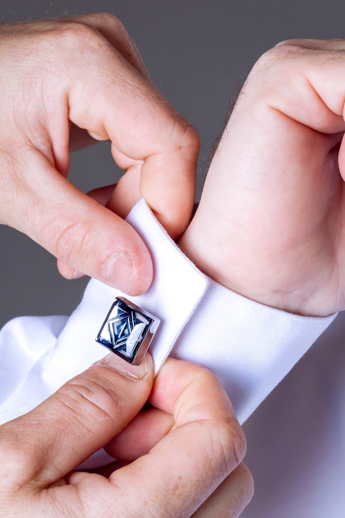 Detailed shot of hands adjusting stylish cufflinks on a white dress shirt, showcasing elegance and professionalism.